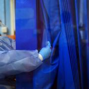 A nurse wearing full PPE adjusts a curtain on a ward for Covid patients